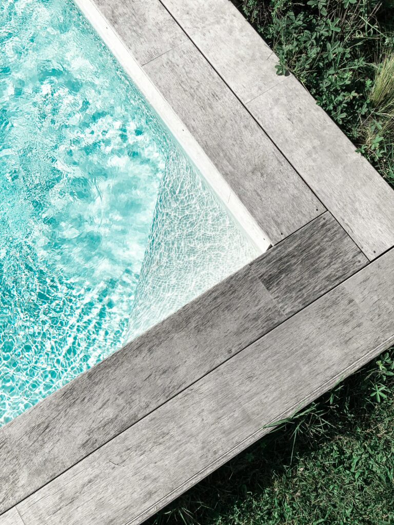Close-up view of a serene swimming pool with wooden decking surrounded by greenery.